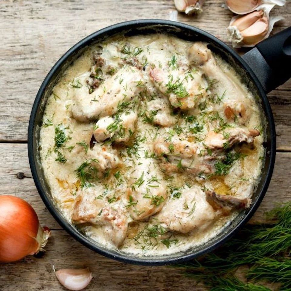 Creamy chicken and mushroom skillet garnished with fresh herbs on a wooden surface.