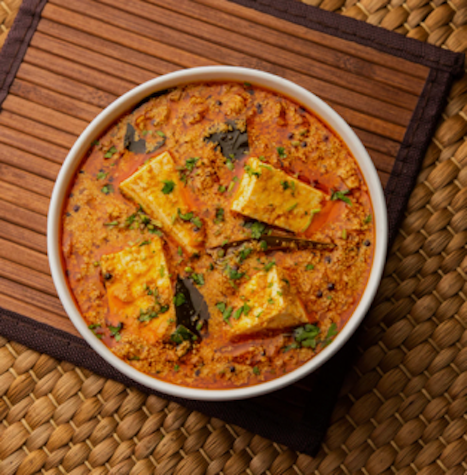 A bowl of Indian paneer curry garnished with chopped cilantro, served on a woven mat.