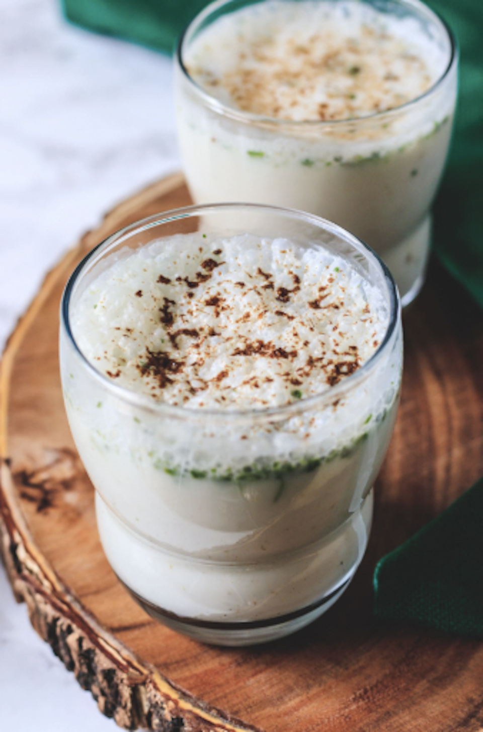 Two glasses of rice pudding topped with cinnamon on a wooden tray.