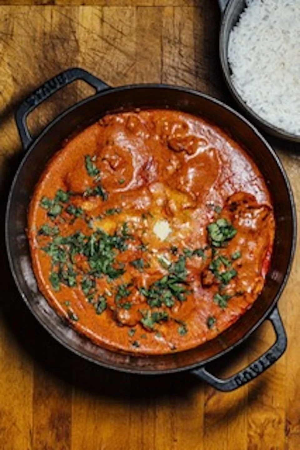 A bowl of red curry garnished with chopped cilantro, accompanied by a plate of white rice.