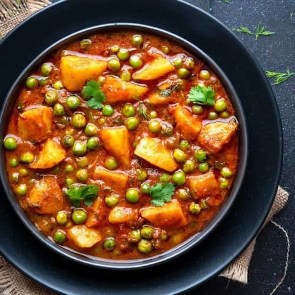 A bowl of spicy potato and green pea curry garnished with cilantro leaves