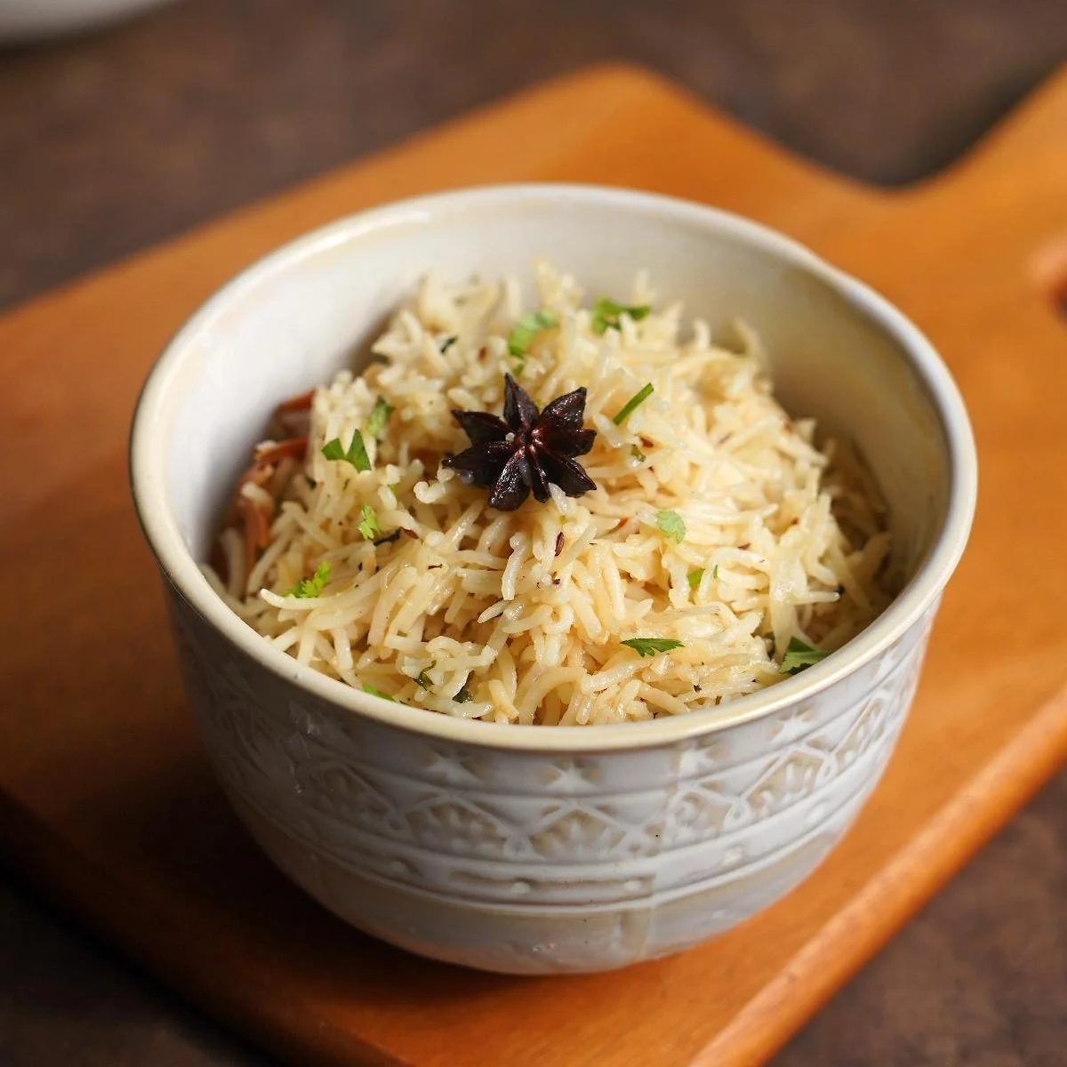 Bowl of cooked rice garnished with fresh herbs and a star anise on top.