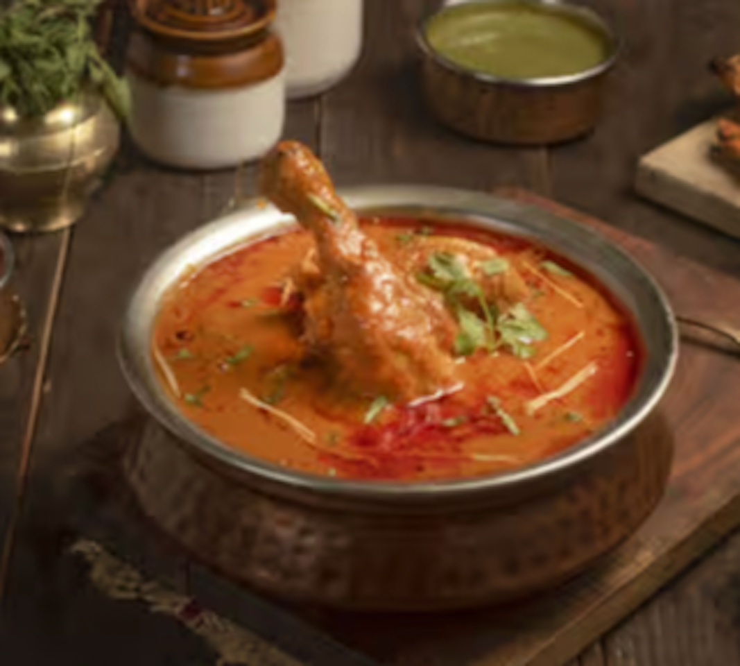 A bowl of chicken curry with a piece of chicken drumstick and garnished with cilantro, served in a silver bowl.