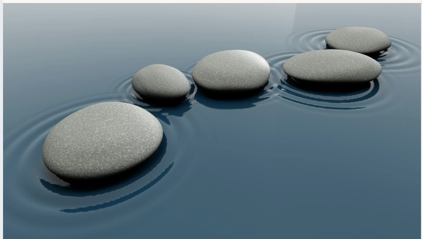 Five gray stones placed in a row on calm water, creating ripples around each stone, with a light gradient sky background.