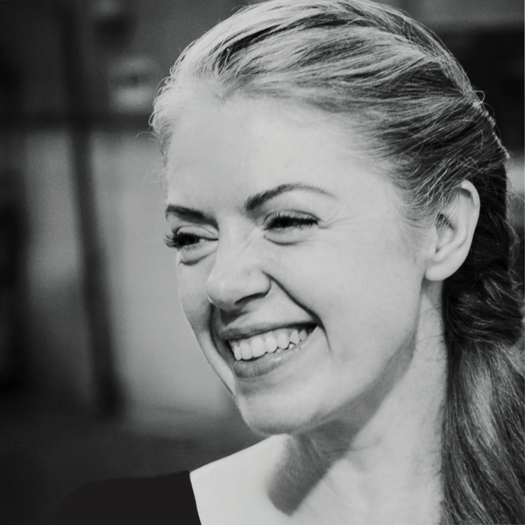 Black and white photo of a smiling woman with hair tied back into a low style.