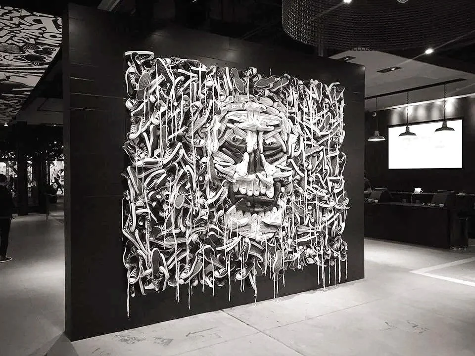 Black and white art installation of a human skull made from hanging sneakers mounted on a black wall.