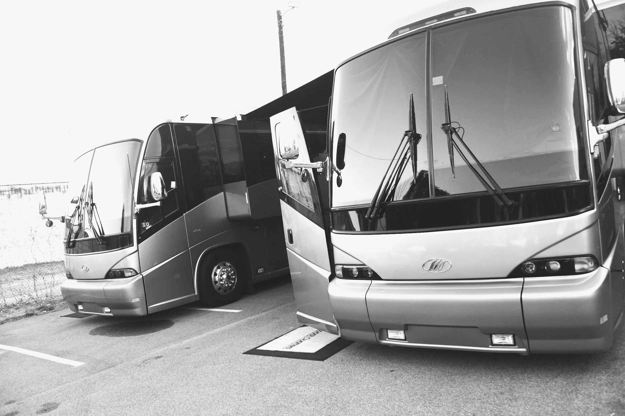 Two tour buses parked closely in a parking lot, with one bus displaying a sign near the door and a ground decal indicating designated parking.