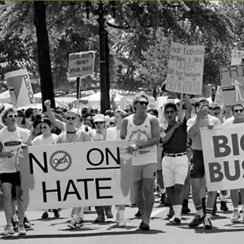 Group of people participating in a march or protest holding signs with anti-hate messages, including a large banner that reads "NO ON HATE."