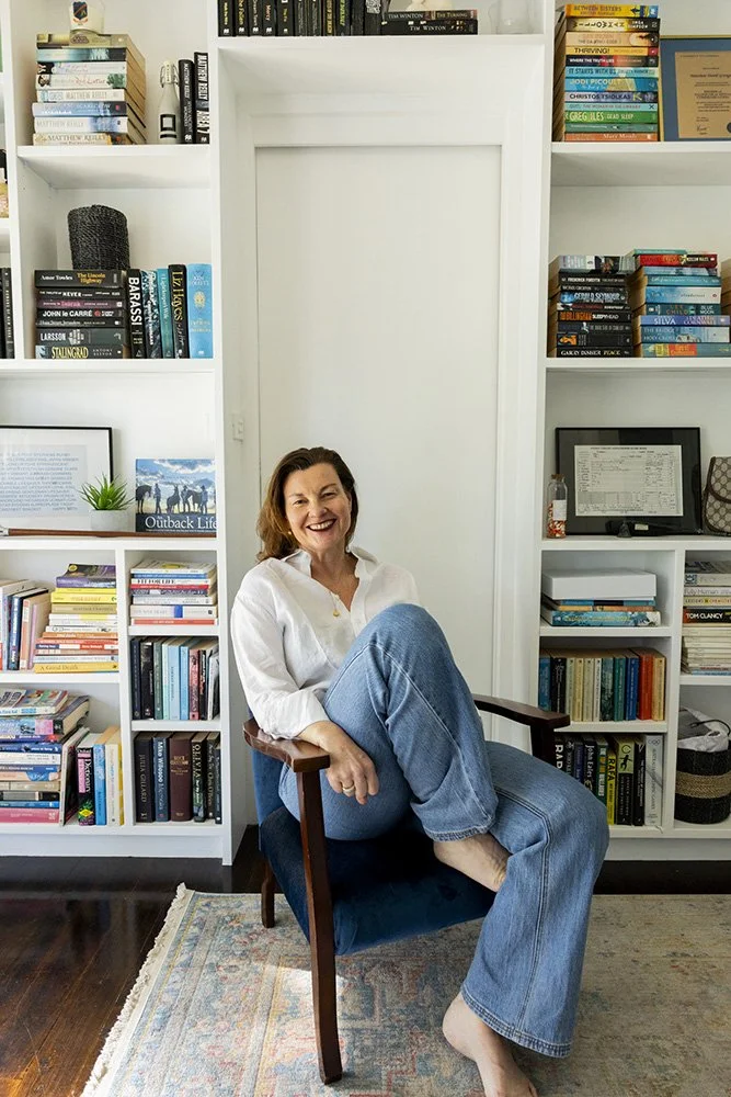 Narelle sitting relaxed on a chair in front of a bookcase