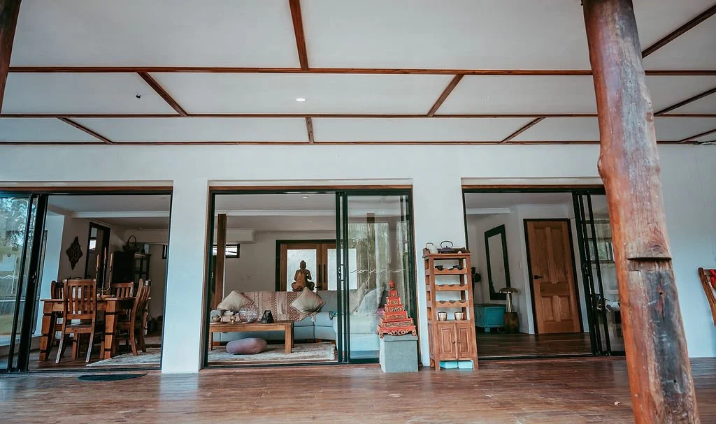 Interior of a modern home with large sliding glass doors, wooden furniture, and Asian decor elements.