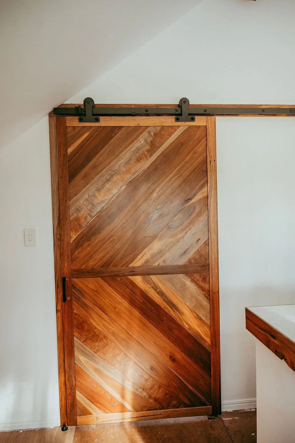 A wooden sliding barn door on a metal track in a room with white walls and a corner cabinet.