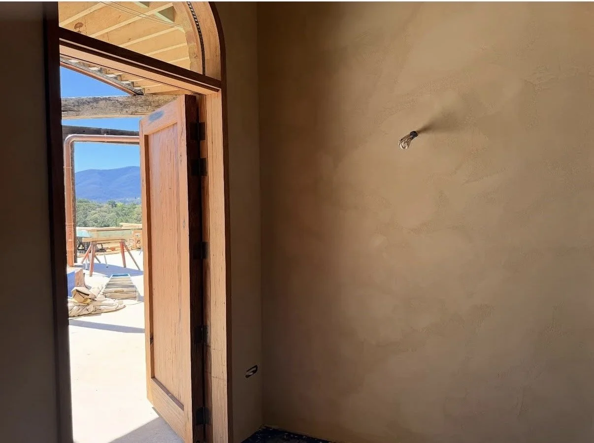 Interior of a room under construction with a wooden door open to an outside view of mountains and clear sky.