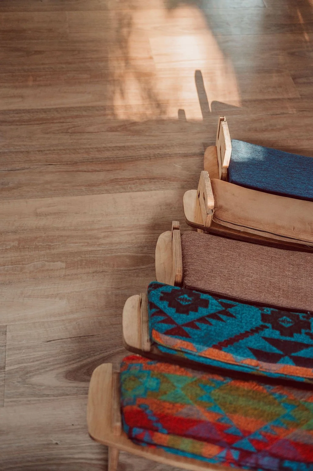 A top-down view of wooden chairs with colorful woven blankets draped over their seats, arranged on a wooden floor.