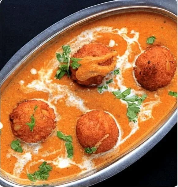 A metal serving dish of Indian chicken curry with four fried chicken pieces and garnished with chopped cilantro.