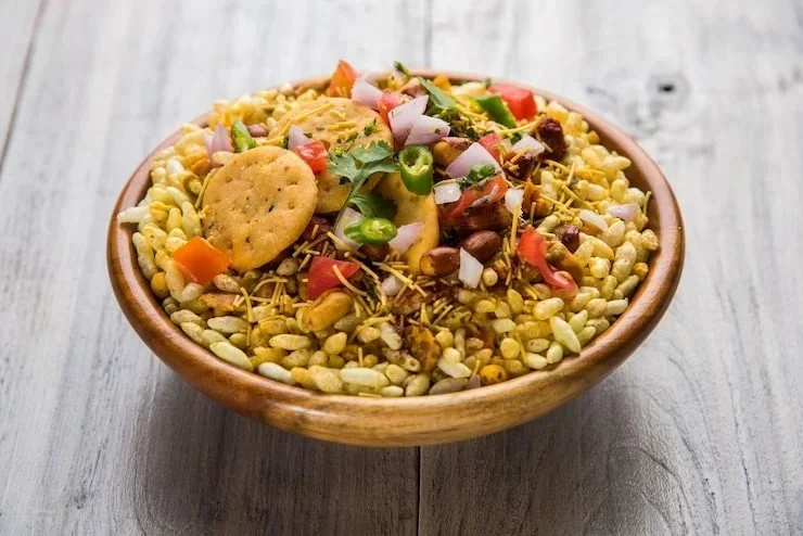 A bowl of bhel puri, an Indian snack with puffed rice, chopped vegetables, and fried snacks.