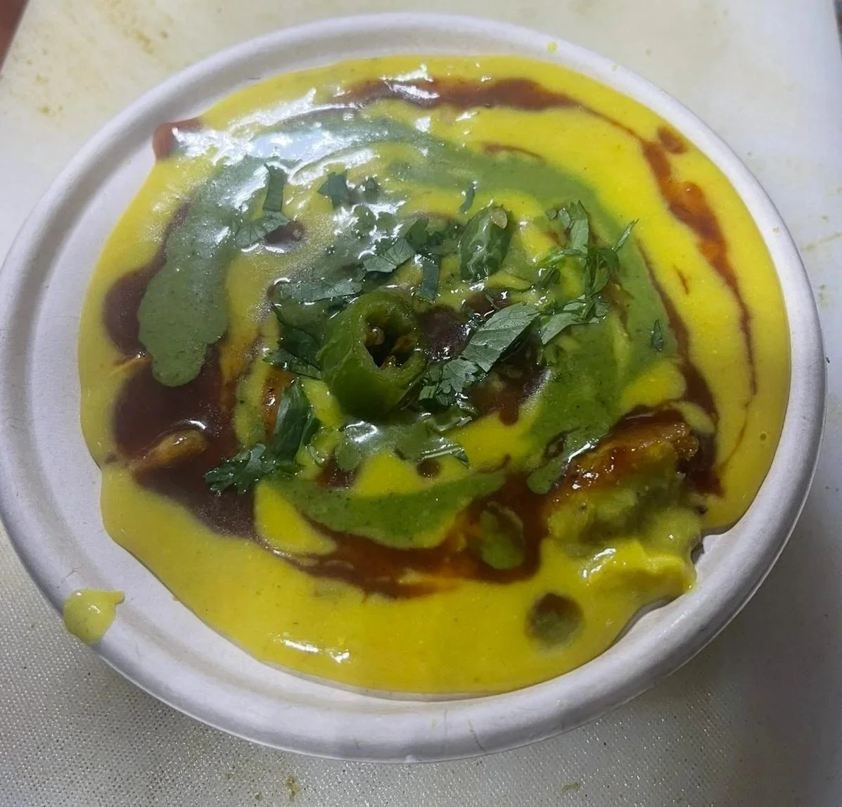 A bowl of Indian curry topped with chopped cilantro and green chili, with yellow and brown sauce swirling.