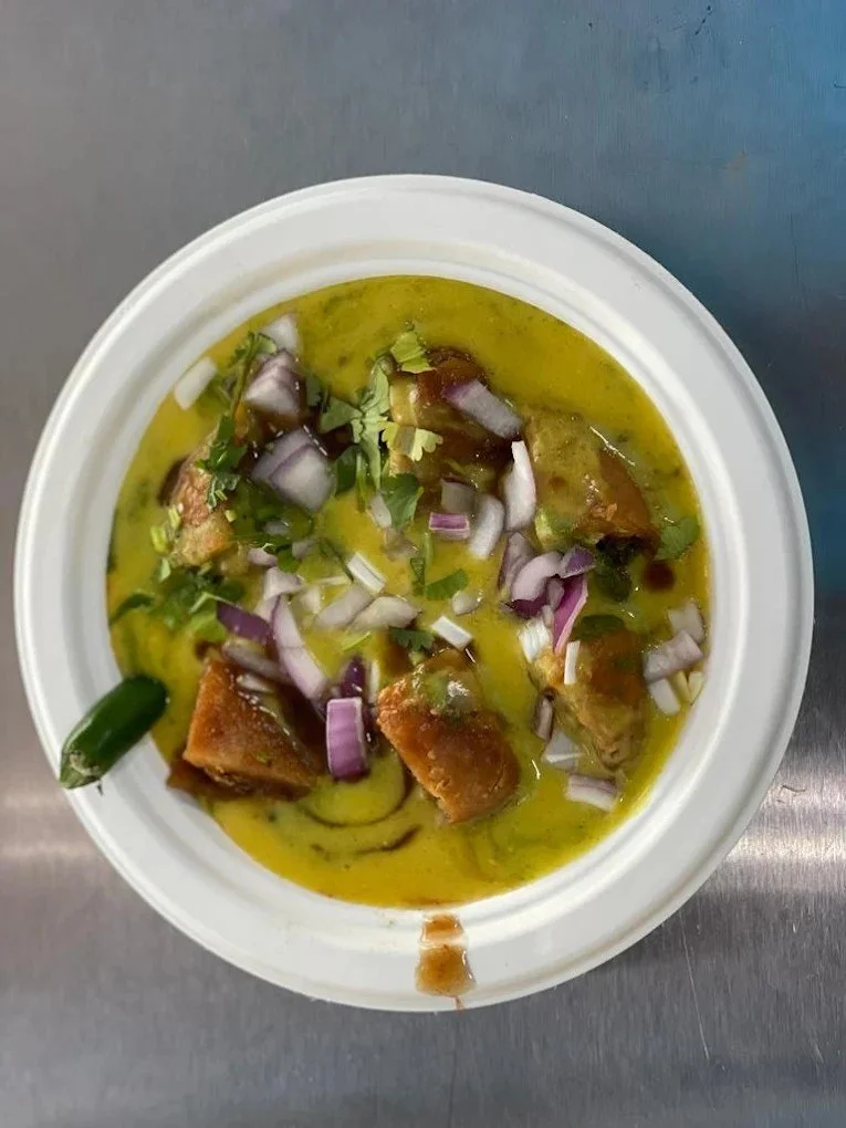 A bowl of Indian fish curry garnished with chopped onions and cilantro, with a green chili on the side.