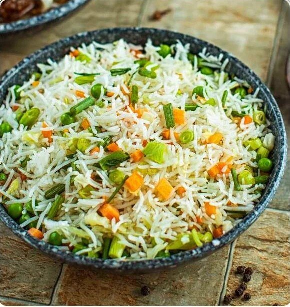 A bowl of cooked rice mixed with chopped green onions, carrots, and other vegetables.