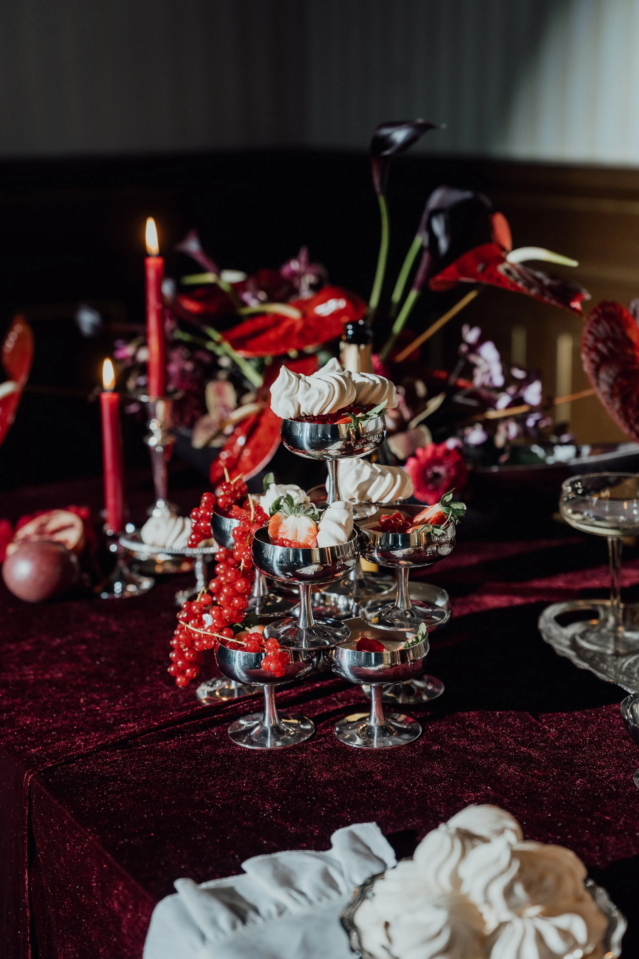 Elegante Desserts und Dekorationen auf einem Festtisch, mit roten Kerzen, roten Beeren und dunklen Blumen.