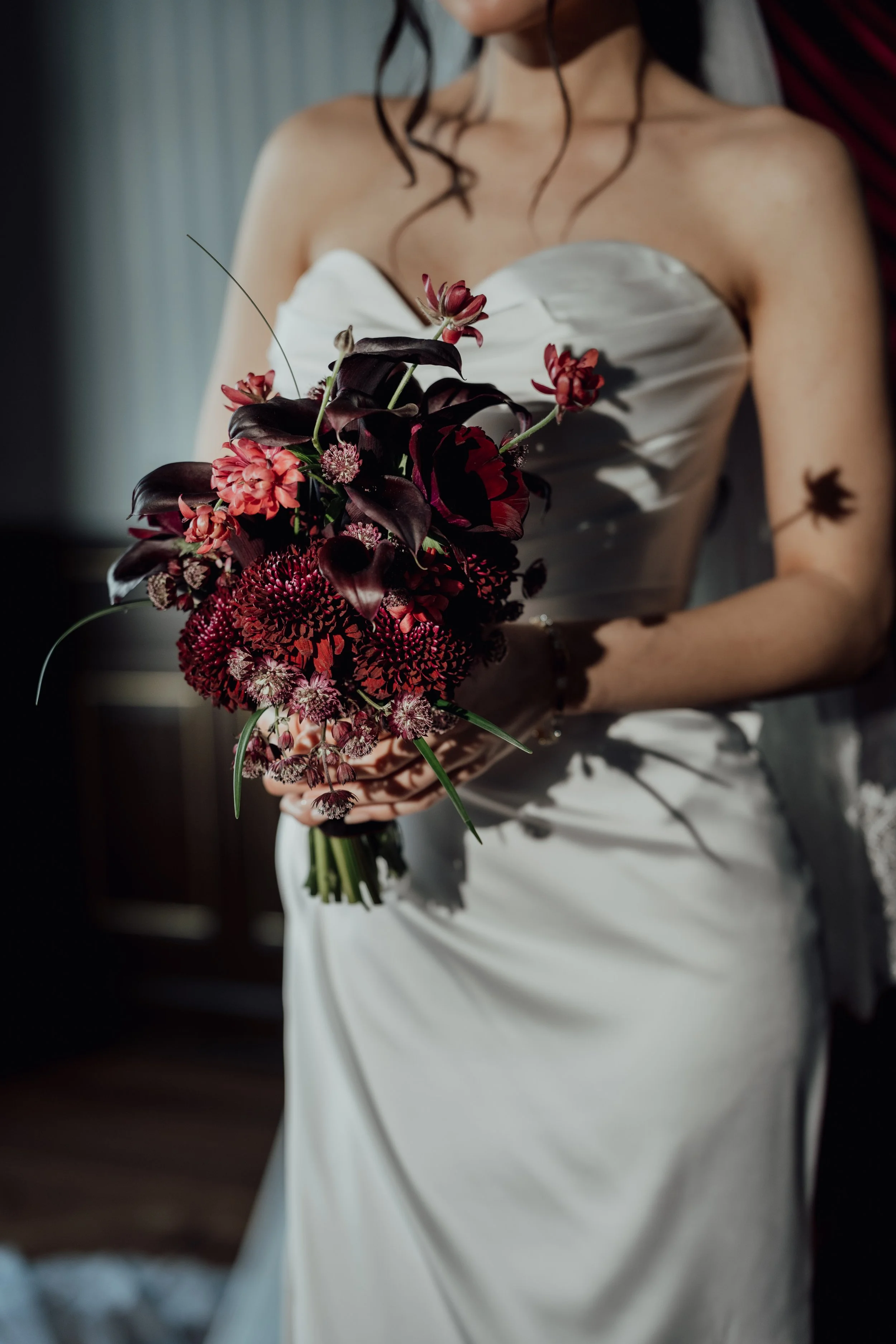 Eine Frau in einem weißen Kleid hält einen Blumenstrauß mit roten und dunklen Blüten.
