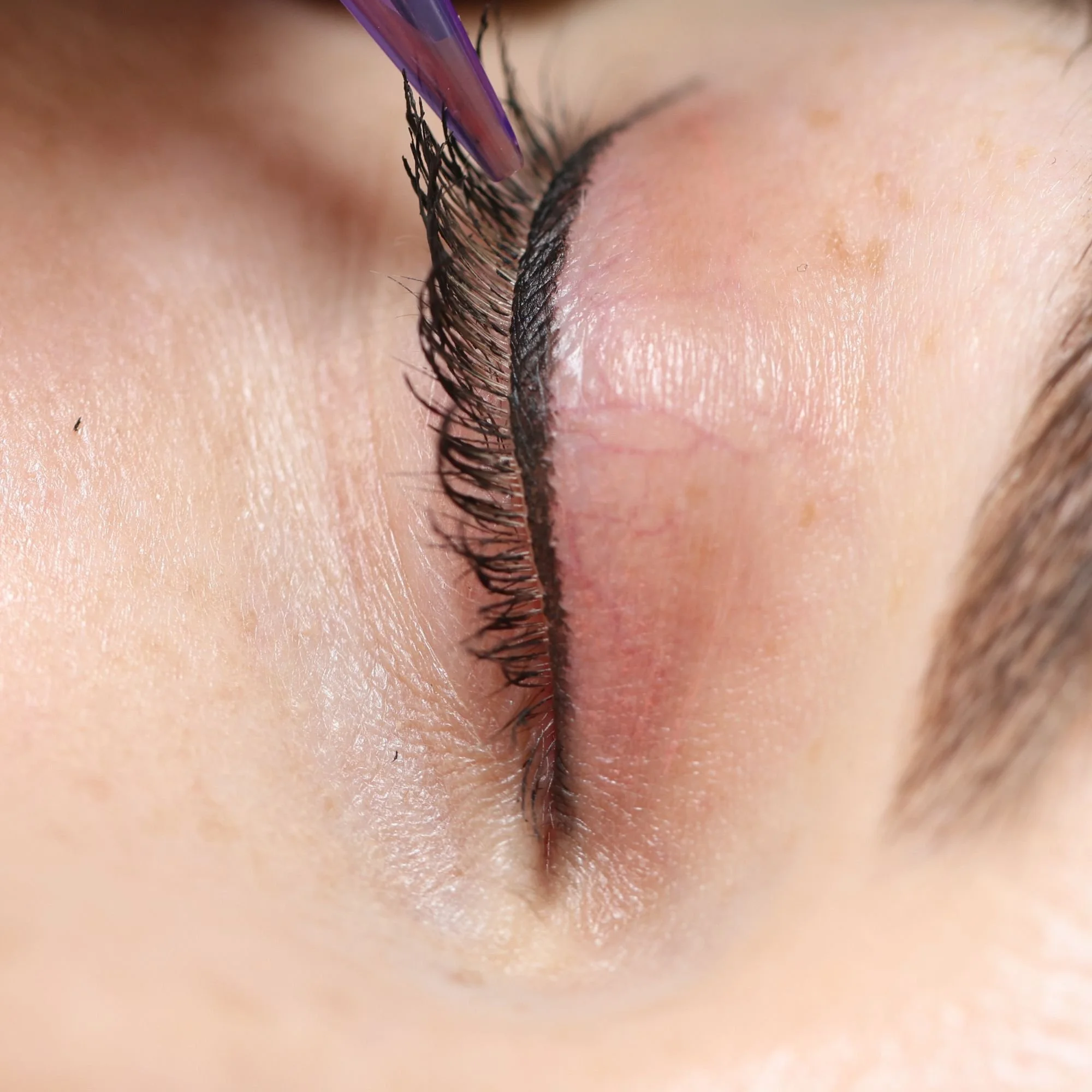 Close-up shot of a person's face with long, natural eyelashes and permanent eyeliner being applied with a PMU pen.