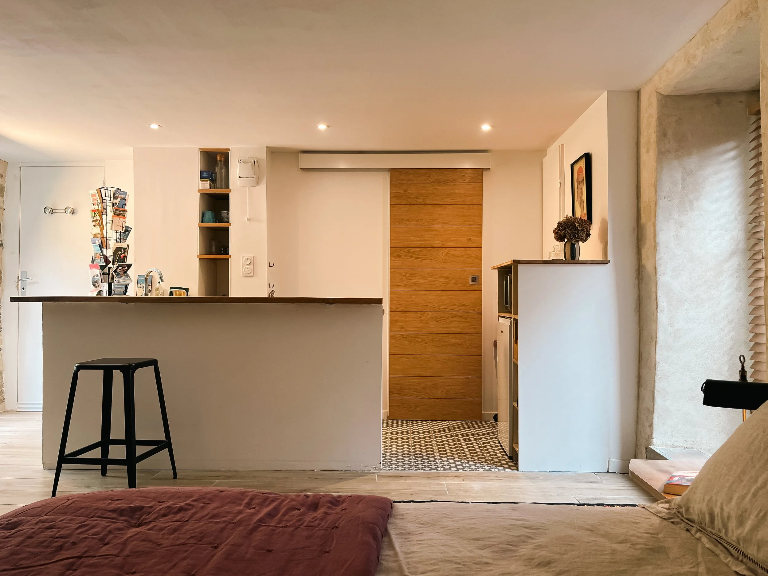 Interior view of a modern living space with a kitchen island, wooden sliding door, decorative vase with flowers, and patterned tiles on the floor near the doorway.