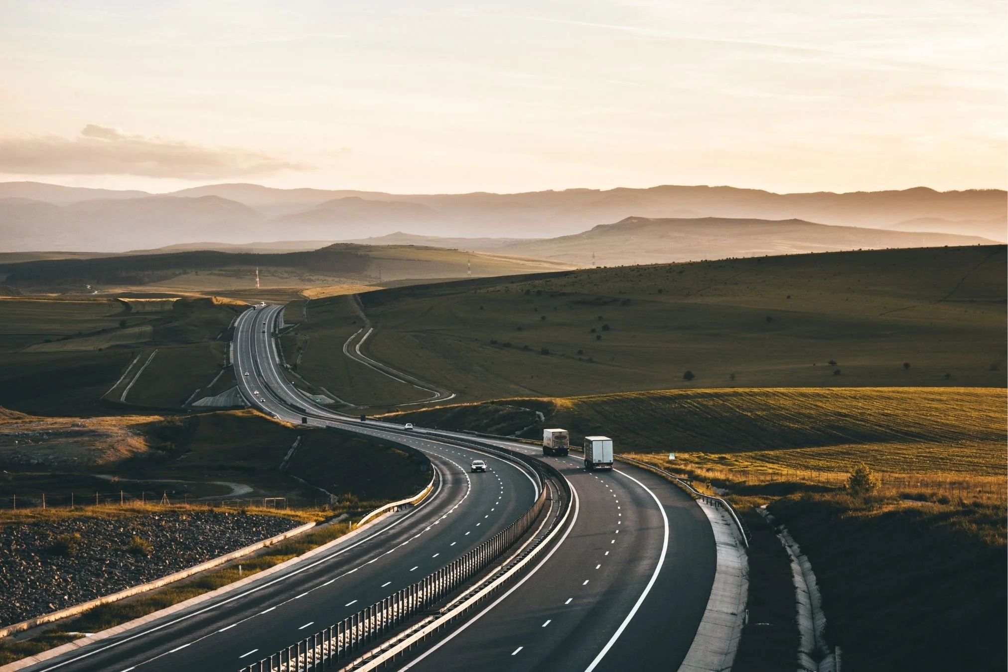 Commercial trucks traveling on a winding highway at sunrise, illustrating factors that influence trucking insurance cost for long-haul carriers.