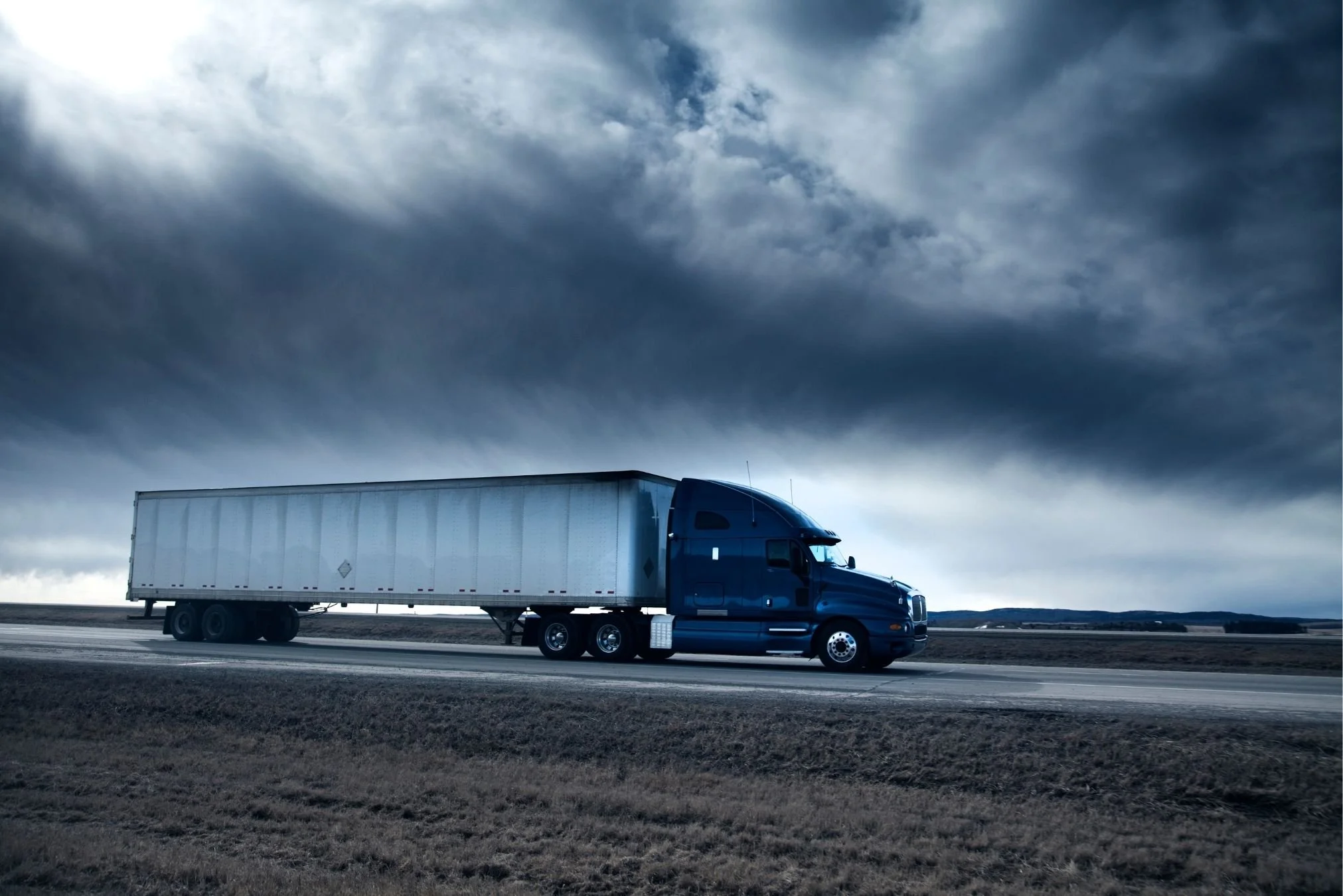 Blue semi-truck operating under changing weather conditions, a key consideration when calculating trucking insurance cost.