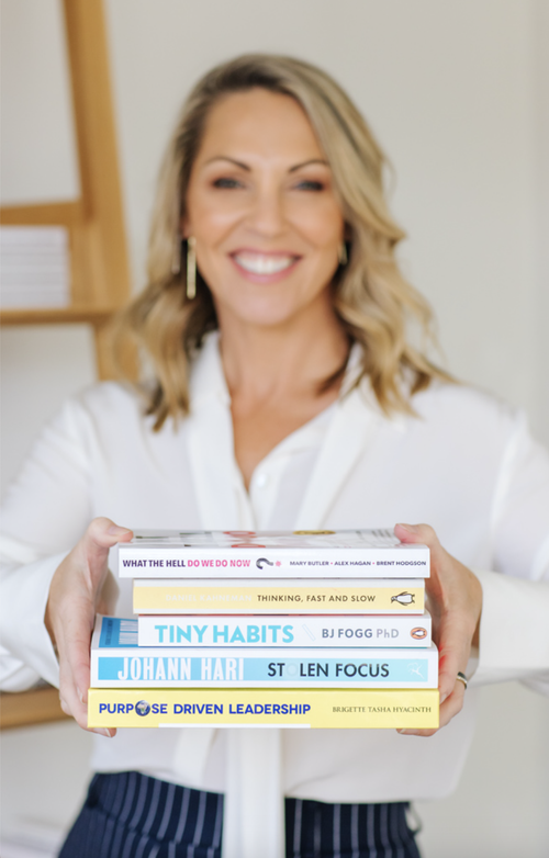 Celeste Halliday holding a stack of the leadership and psychology books she recommends most
