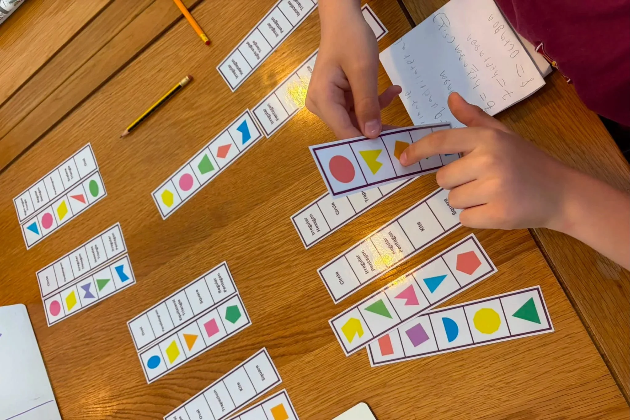 People playing a board game with colorful shape cards on a wooden table.