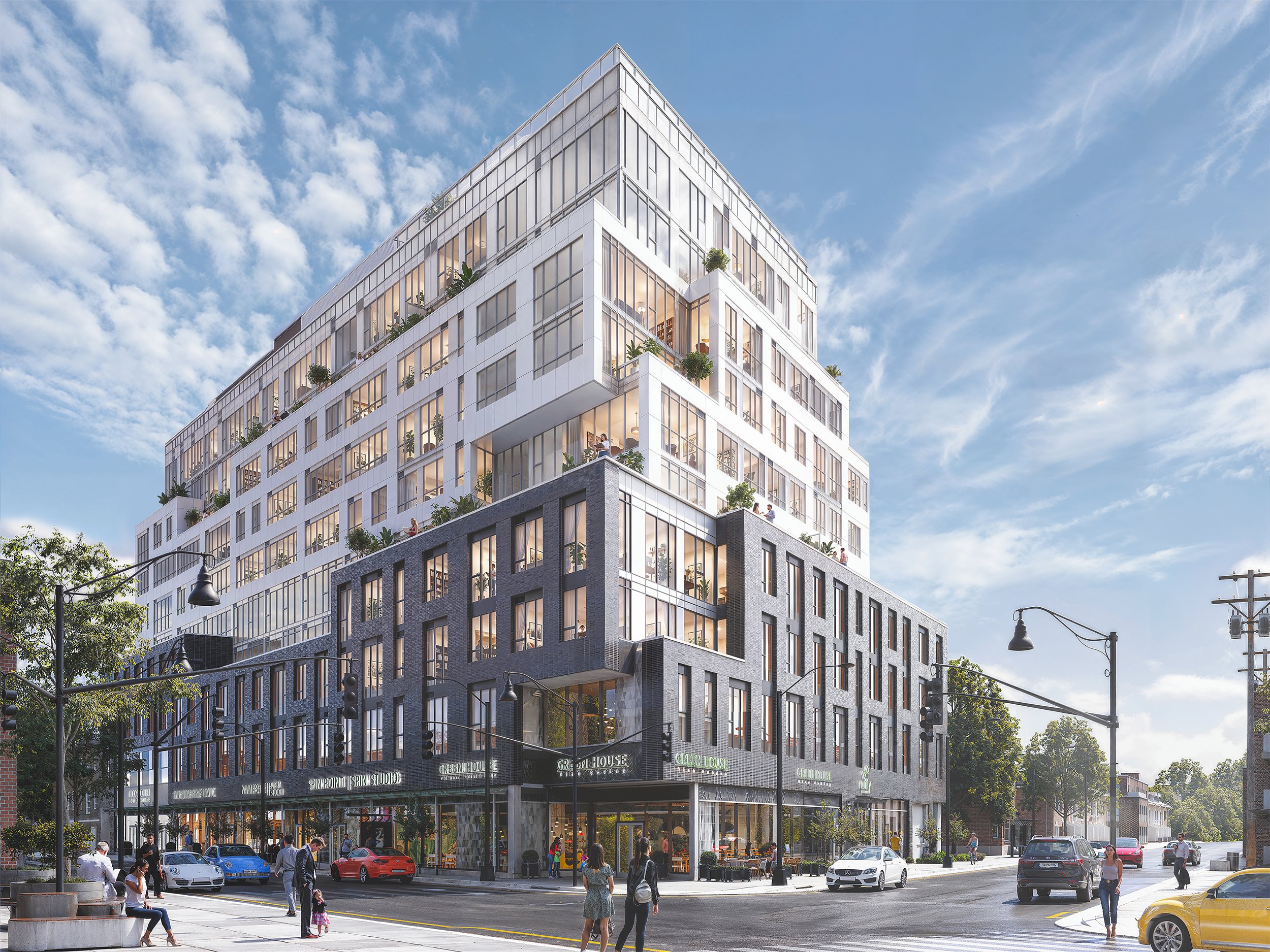 A modern multi-story building with large glass windows and balconies, situated at a busy street corner with people walking and cars parked nearby. The building has commercial spaces on the ground floor and residential or office spaces above, with a blue sky and some trees in the background.
