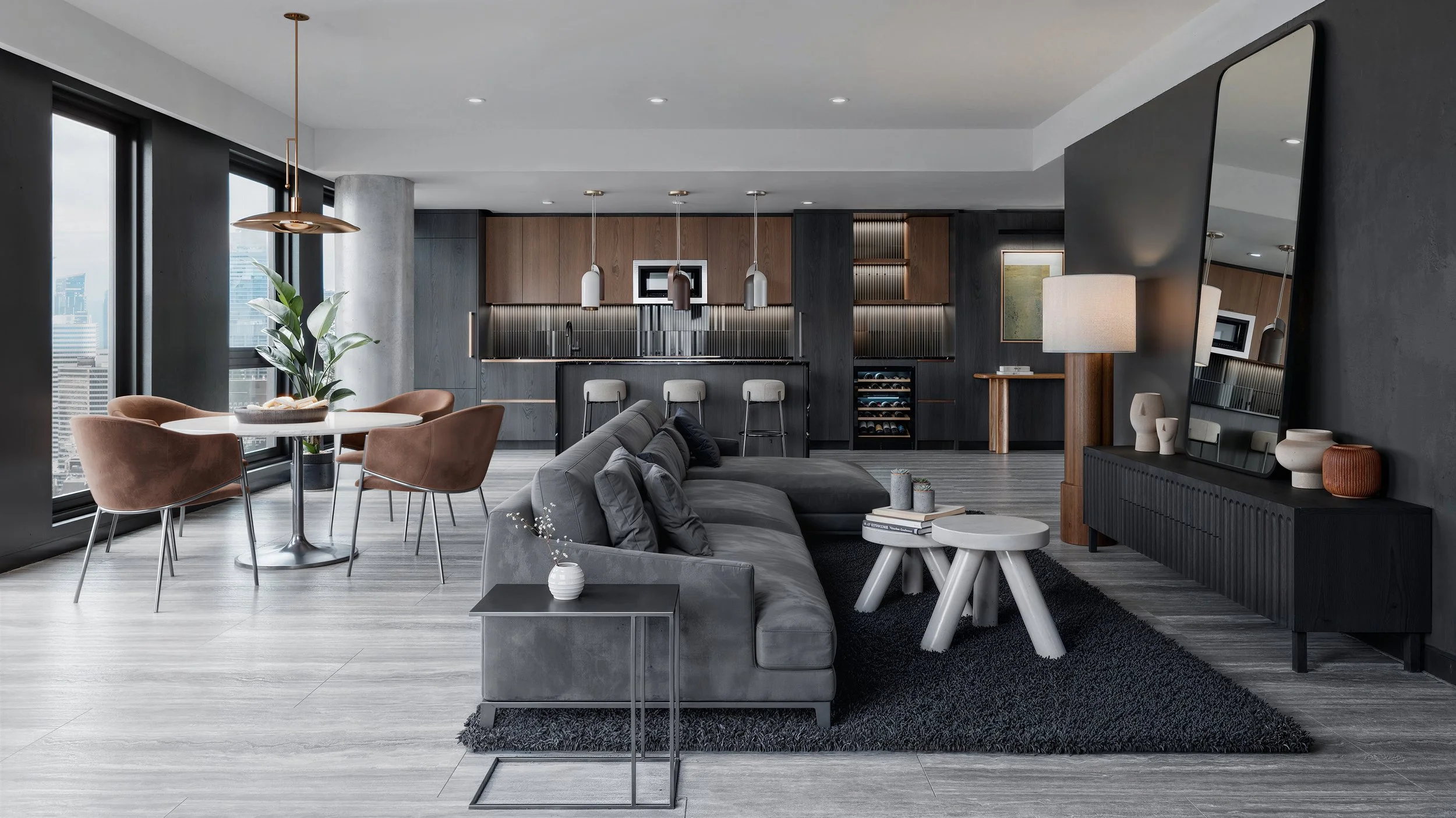 Modern open-plan living room with gray sofa, black shag rug, white side tables, decorative vases, and a large mirror, adjacent to a dining area with a round table and pink chairs, overlooking city skyscrapers through large windows, with a contemporary kitchen in the background.