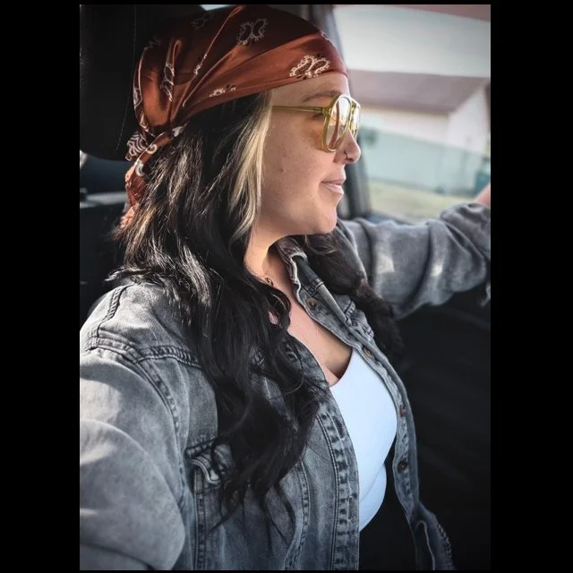 Woman with long dark hair, wearing sunglasses and a red bandana, driving a car