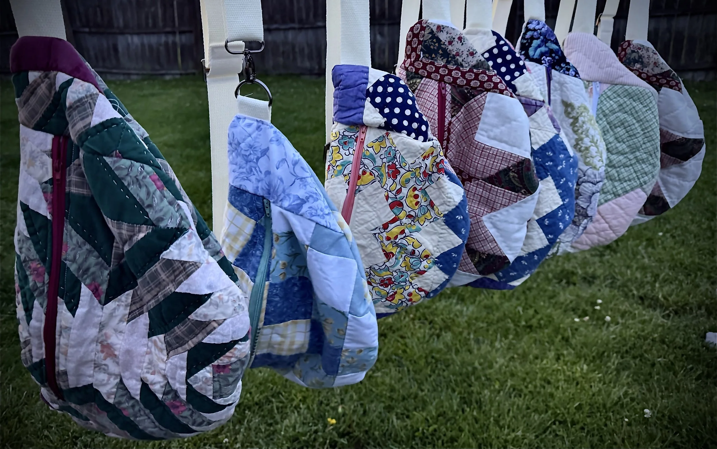 Colorful patchwork quilts hanging on a clothesline outdoors in a grassy yard.