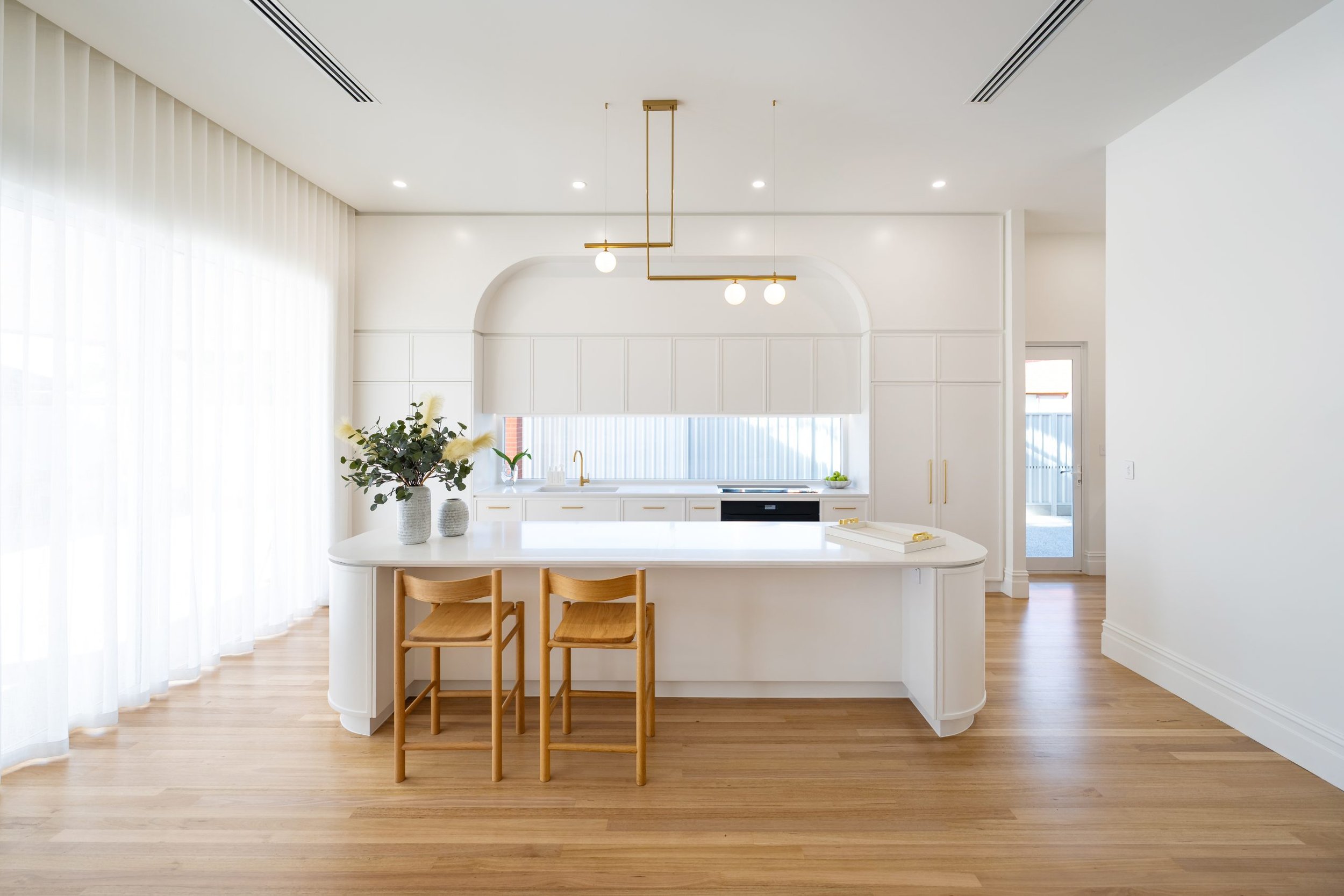 Bright, modern kitchen with white cabinets, a white island with a curved edge in Zenith Surfaces by Stone Ambassador White Truffle mineral stone