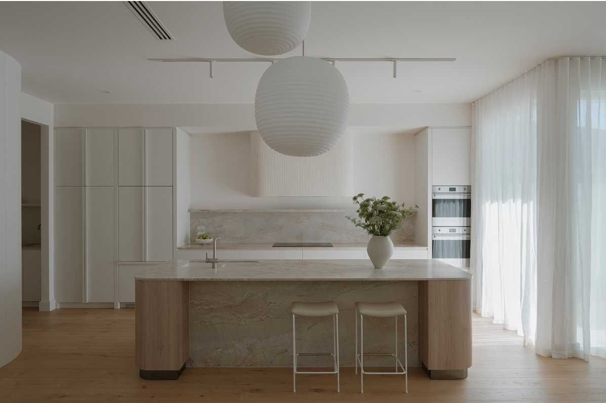 Modern minimalist kitchen with white cabinetry, marble island, and large white pendant lights, bright with natural light and sheer curtains.