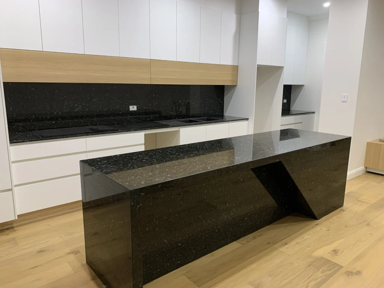 Modern kitchen with black granite stone tops, white cabinetry, and a large bespoke black granite island. The black granite splashback adds to this statement kitchen.