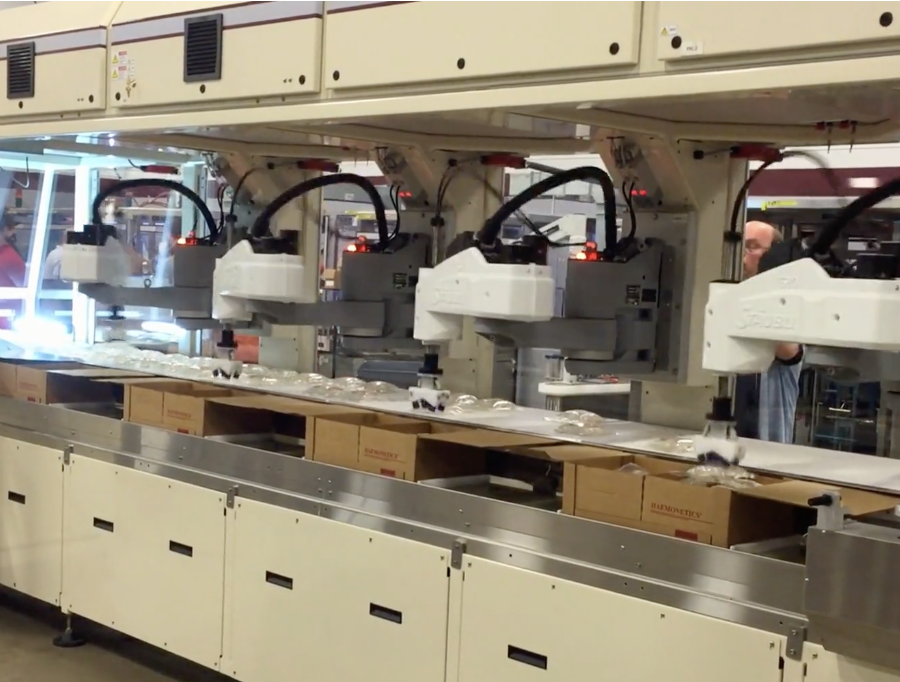 Industrial packaging line with robotic arms sealing plastic bags into boxes in a factory setting.