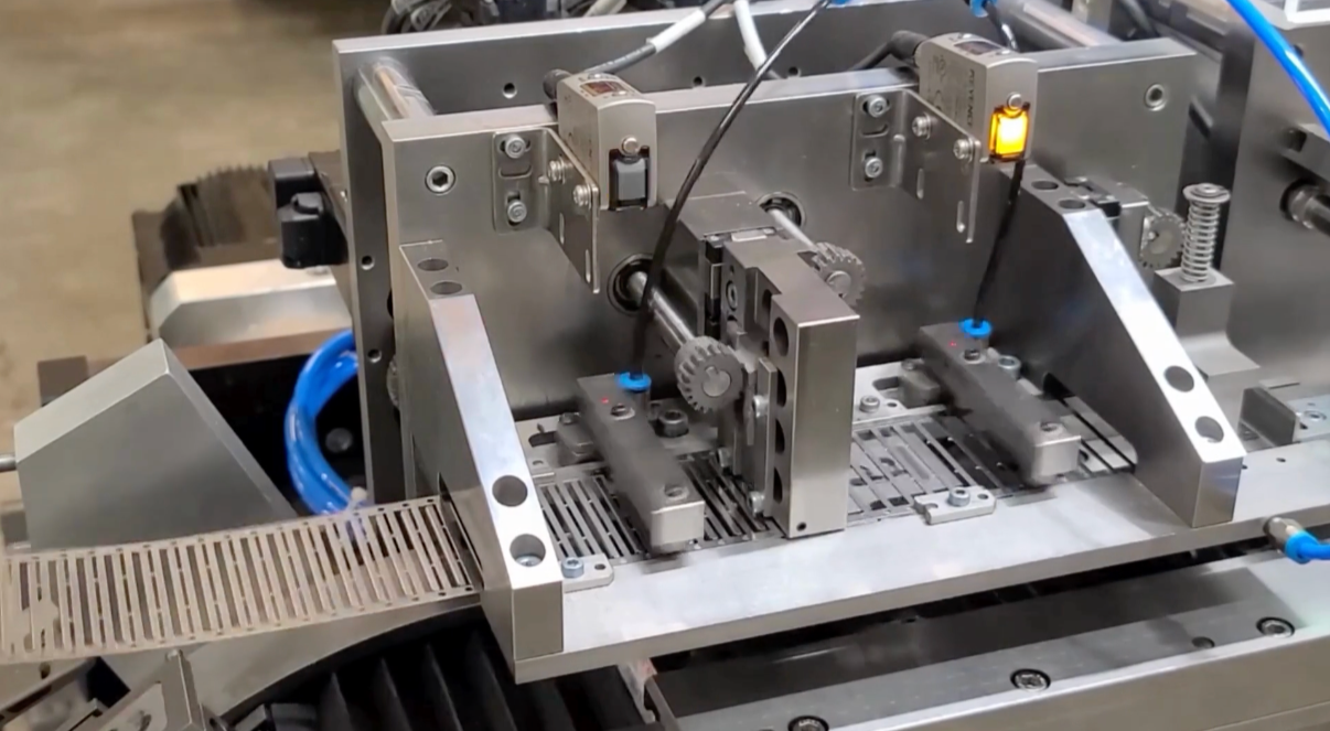 Close-up of industrial robotic machinery with metal components, gears, and a conveyor belt, used for manufacturing automation.