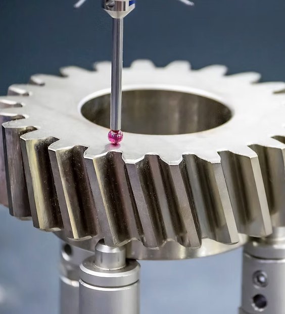 Close-up of a metallic gear with a pink-colored tiny sphere being placed on top by a precision tool, with a mechanical setup underneath.