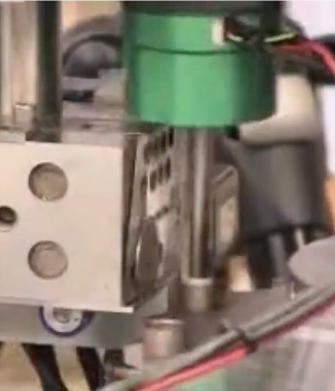 Close-up of an industrial or mechanical device with metallic parts, green component, and black wires.