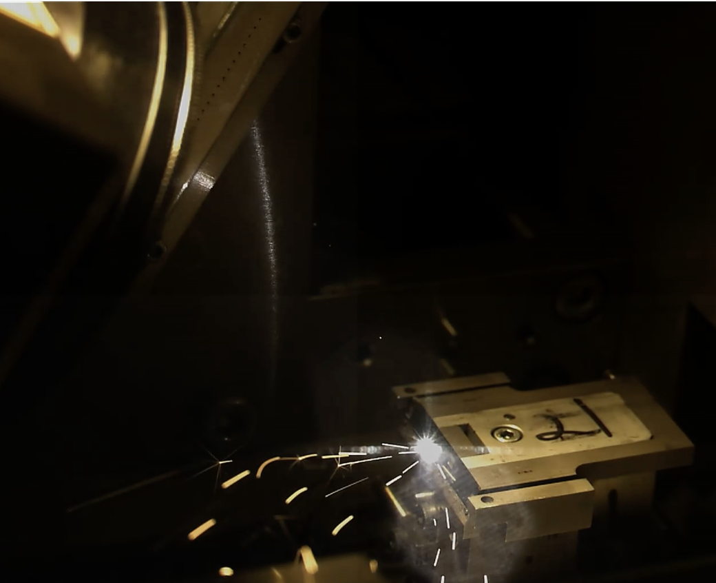 A metal machine part is being cut or welded, producing bright sparks in a dark environment.
