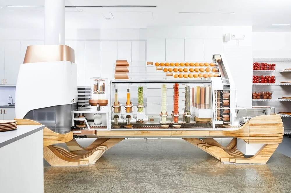 Modern pastry display case with wood accents, showcasing various pastries, eggs, and ingredients in a bright, sleek bakery or cafe.