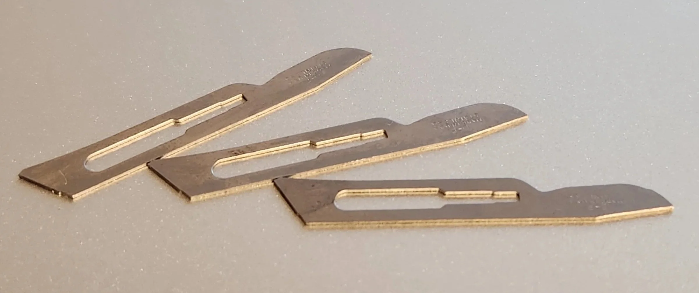 Three metal razors with a cutout in the center, arranged on a gray surface.