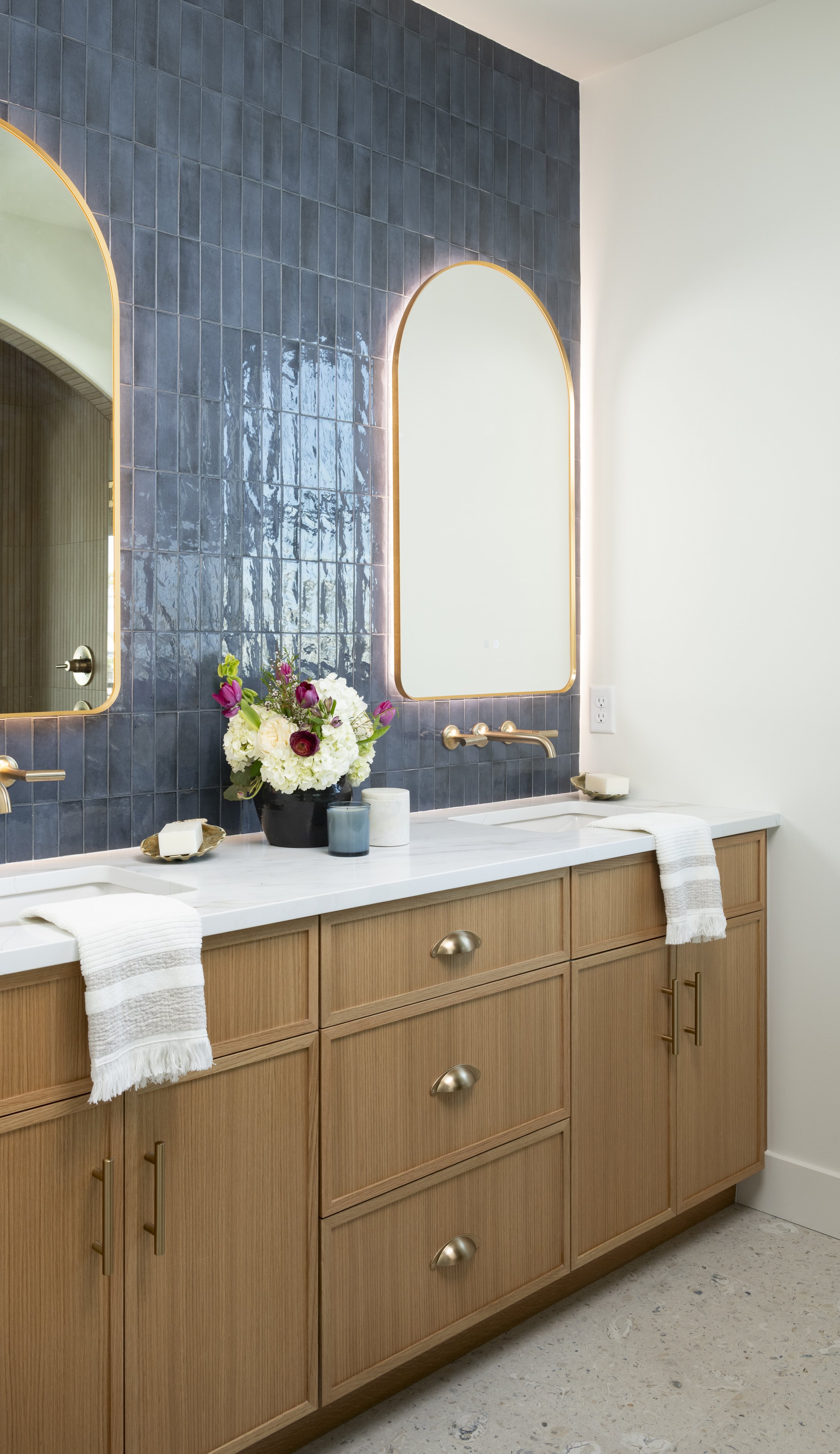Custom white oak vanity with illuminated mirrors, designer tile, and premium fixtures in a luxury master bathroom.