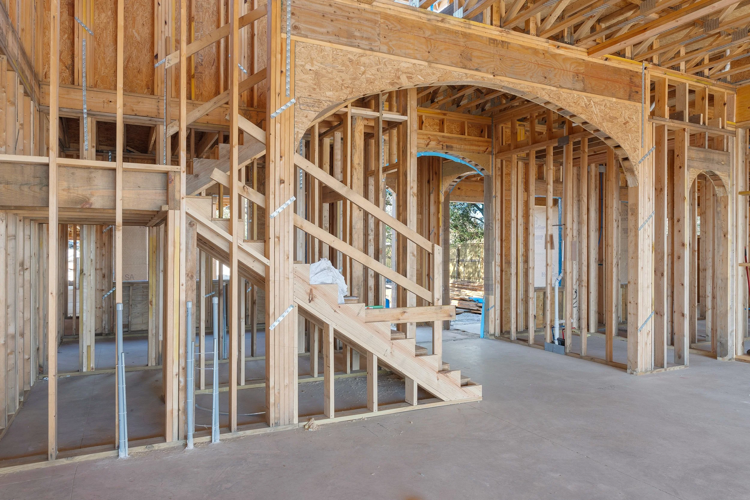 Interior of a building under construction with wooden framing, stairs, and arched support beams.