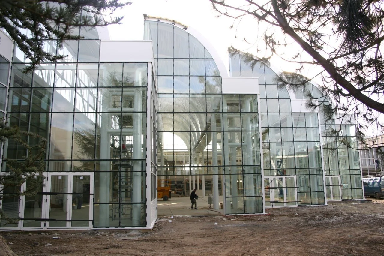 Bâtiment moderne en verre en construction, avec des structures en cours d'installation, et des personnes travaillant à l'extérieur.