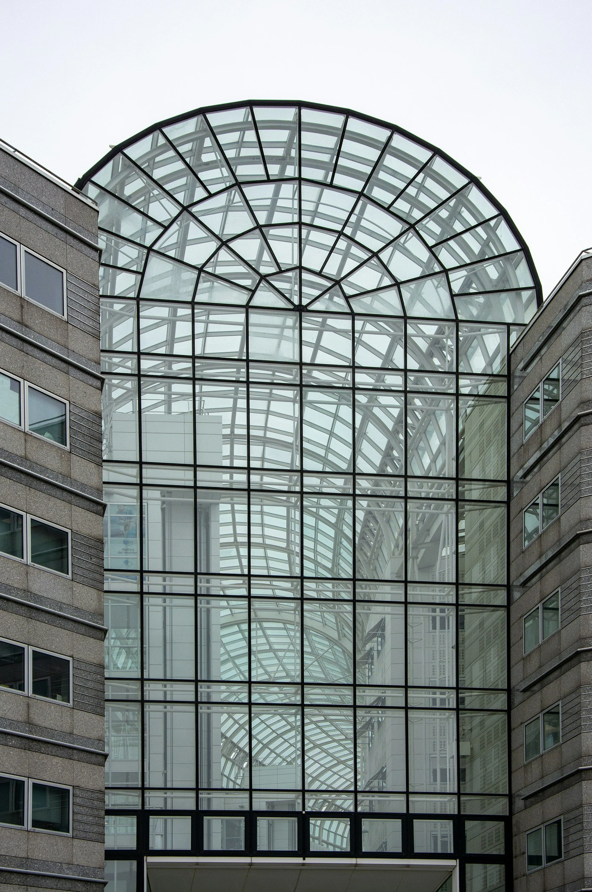 Un bâtiment moderne avec une grande structure en verre en forme d'arche reliant deux côtés en béton.