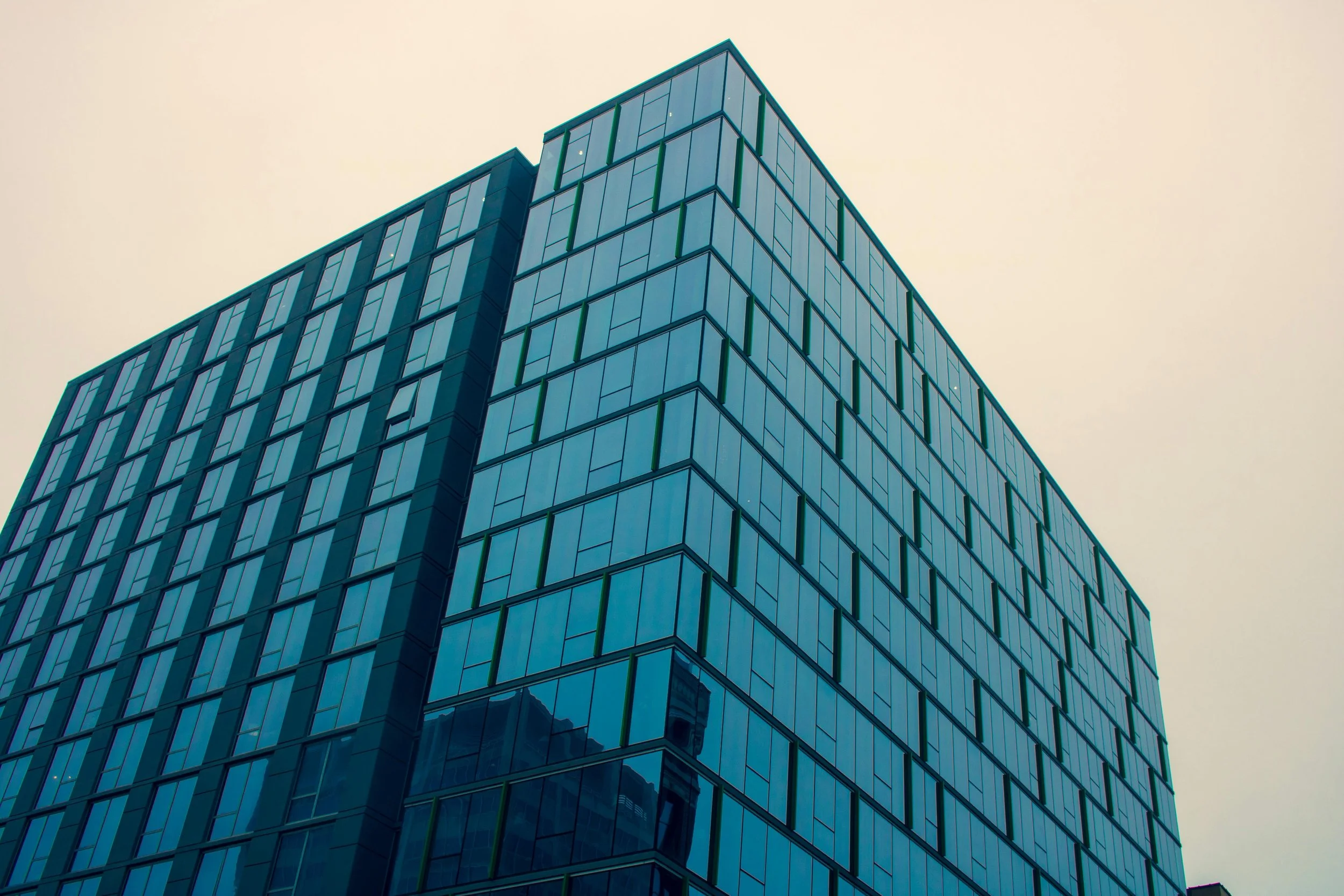 Vue d'un bâtiment moderne en verre avec plusieurs fenêtres, vu en contre-plongée, sous un ciel clair.
