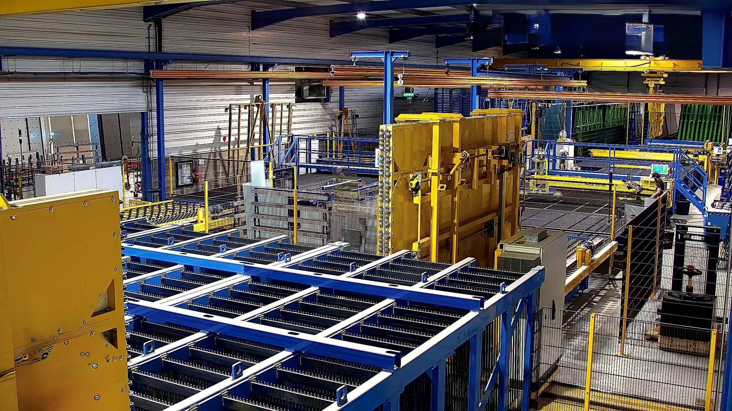 Centre de tri avec des structures métalliques bleues et jaunes, des rails, et des équipements automatisés pour la manipulation de plaques de verre